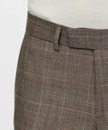 Close-up of brown plaid trousers with a belt loop and pleated detail, worn with a white shirt.