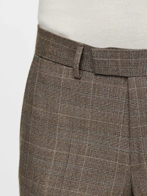 Close-up of brown plaid trousers with a belt loop and pleated detail, worn with a white shirt.