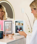 Woman using Dope Portable 4L Mini Fridge and Cooler Warmer, pink finish, on a vanity for skincare products.