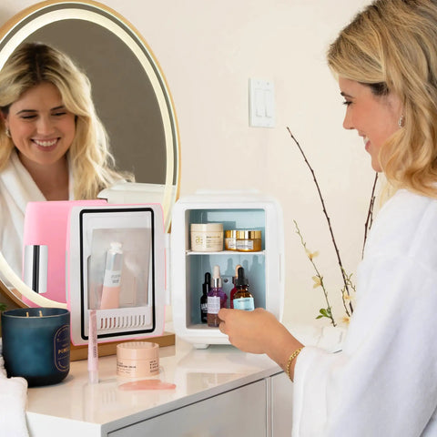 Woman using Dope Portable 4L Mini Fridge and Cooler Warmer, pink finish, on a vanity for skincare products.