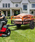 Man towing Beefy ATV Dump Cart With 1500 Lbs Capacity, Tow Behind Garden Trailer With Removable Sides loaded with bags on lawn