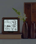 Backlit Wireless Forecast Weather Station With Pressure And Temp Trends Indoor Outdoor Temp Humidity 24 Hour Pressure History Temperature Alerts And Continuous Display placed on a book beside decorative vases.