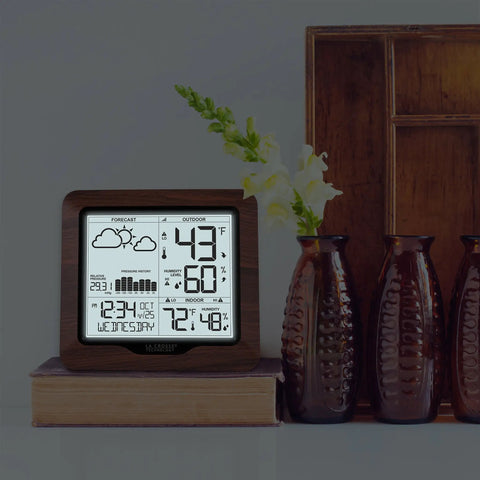 Backlit Wireless Forecast Weather Station With Pressure And Temp Trends Indoor Outdoor Temp Humidity 24 Hour Pressure History Temperature Alerts And Continuous Display placed on a book beside decorative vases.