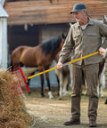 Man using Manure Fork With 18 Angled Tines Long Fiberglass Handle Muck Rake Tool For Garden And Farm Cleanup in a stable