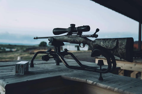 Stinger Adjustable Ambidextrous Rifle Shooting Rest With Lightweight Build For Rock Solid Stability Outdoors And Range No Wobble Elevation System Cam Over Front Rest Locks Steel Tube Frame holding a rifle on a wooden table outdoors.
