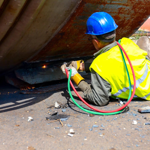 Worker using Oxy Acetylene Torch Hose Twin Cutting 25 Ft By One Quarter Inch B Fitting Welding Gas Hose under large metal structure.