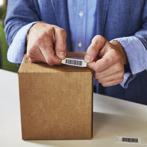 No Sweat Multi Purpose Thermal Labels For Labelwriter Printers 1 By 2 1 8 Inch being applied to a shipping box by hands.