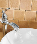 Chrome Vessel Sink Faucet With Waterfall Spout Pop Up Drain Supply Hose And Single Handle Lavatory Mixer Tap For Tall Body Bathroom Setup Slick Solid Brass Build With Ceramic Cartridge For Leak Free Performance in use with water flowing into a white basin against a tile background.
