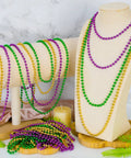 Mardi Gras Beads Necklaces 24 Pack, 33 Inch Round Beads In Green Purple Gold displayed on stands, carnival party favors