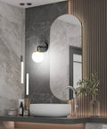 Bathroom with Black And Gold Globe Wall Sconce Mid Century Modern One Light Fixture beside mirror, 6000K G9 bulbs included.