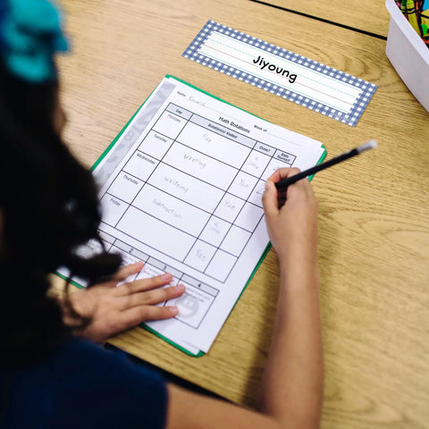Child writing at desk with Farmers Market Desk Labels For Kids 36 Pack Name Tags For Desks And Lockers Classroom Organization visible.