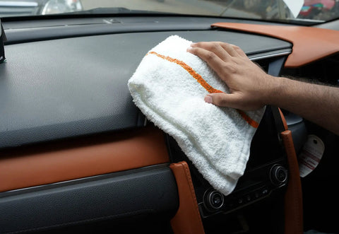 60 Pack 16 By 19 Inch Terry Bar Mop Rags For Cleaning Absorbent And Durable Cotton Cloths Multipurpose Shop Towels Reusable Rags For Home Office Garage Kitchen And More. White cotton rag with an orange stripe wiping a car dashboard.
