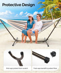 Two people sitting on a hammock supported by a 550 Lbs Capacity Hammock Stand With Portable Carrying Bag Heavy Duty Two Person Frame For Outdoors And Indoors Black Antique Finish Sturdy Steel Construction on a beach.