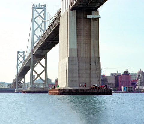 Bay Bridge foundation view over water with city skyline in background, showcasing structural engineering details.