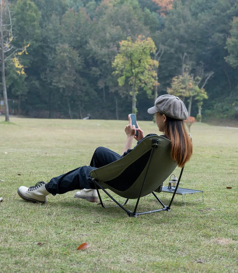 Ultralight Low Profile Camping Folding Chair with Side Pocket and Carry Bag 7.5 Inch Seat Height Ultra Compact and Stable on Uneven Ground Ideal for Backpacking Beach Trips and Outdoor Lounging, shown in use on grass with person relaxing