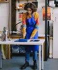 Person using Blue Multi-Surface Painter's Tape 0.94 In X 60 Yds, 6 Rolls, in art studio, wearing blue apron and colorful sweater
