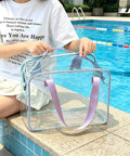 Poolside view of transparent Dry Wet Separated Storage Bag for Gym and Beach Gear, with separate compartments and purple straps.