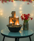 Indoor Tabletop Tiered Water Fountain With 3 Candles, 11 Inch Brown on glass table with flowers and string lights