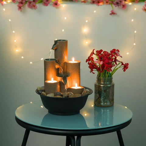 Indoor Tabletop Tiered Water Fountain With 3 Candles, 11 Inch Brown on glass table with flowers and string lights