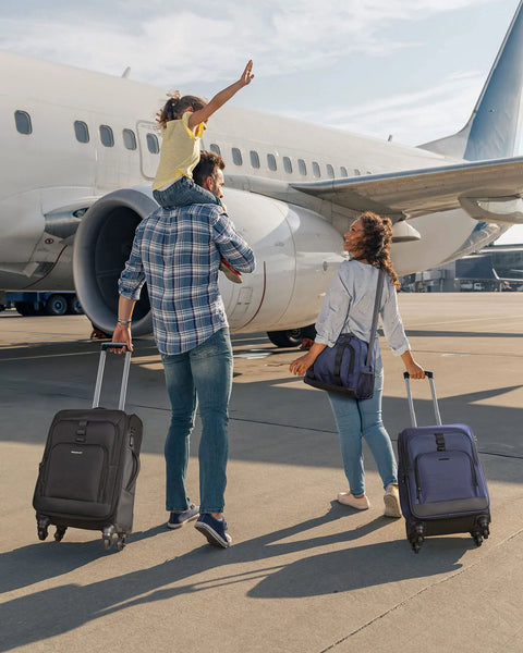 Two 20-inch expandable carry-on suitcases with spinner wheels, black and blue, on an airport tarmac beside a family.