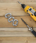 Three 8mm stainless steel quick links for boat anchor chain repair, shown with a yellow cordless drill on wood