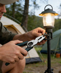 Person using versatile 9-in-1 cutting pliers for wire cutting on outdoor lamp in camping setting with tents visible.