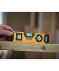 Hand holding 9 Inch Extruded Torpedo Level with durable rigid body and precise vial for fast layout checks on wooden beam.