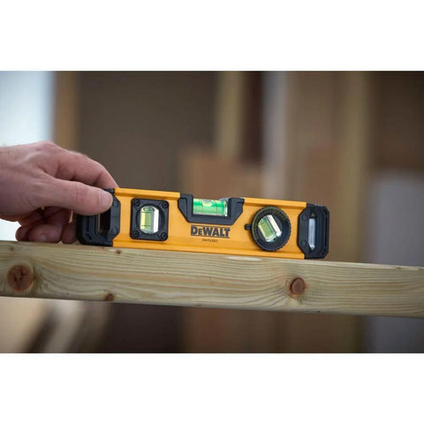 Hand holding 9 Inch Extruded Torpedo Level with durable rigid body and precise vial for fast layout checks on wooden beam.