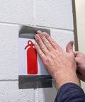 Person applying Value Thin Silver Duct Tape Single Roll to secure a fire extinguisher sign on a wall.