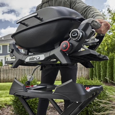 Person setting grill on Portable Folding Grill Cart With All Terrain Wheels For On The Go Grillin Heavy Duty Strap Keeps Your Grill Secured Top Loading Design Upright Lock Indicator And Built In Transport Handle For Easy Mobility.