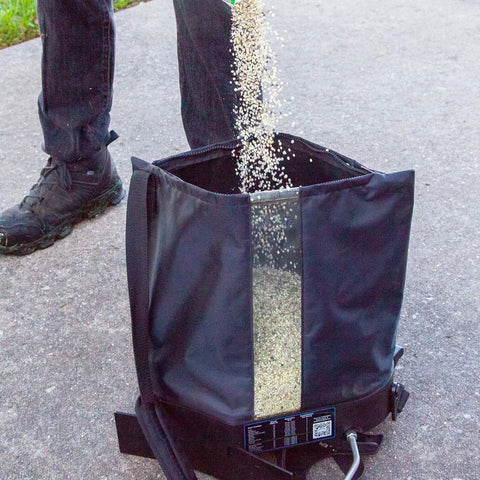 Pouring material into Spyker All Season Spreader Kit Ergo Pro 50 Pound Broadcast Spreader With 25 Pound Bag for lawn care