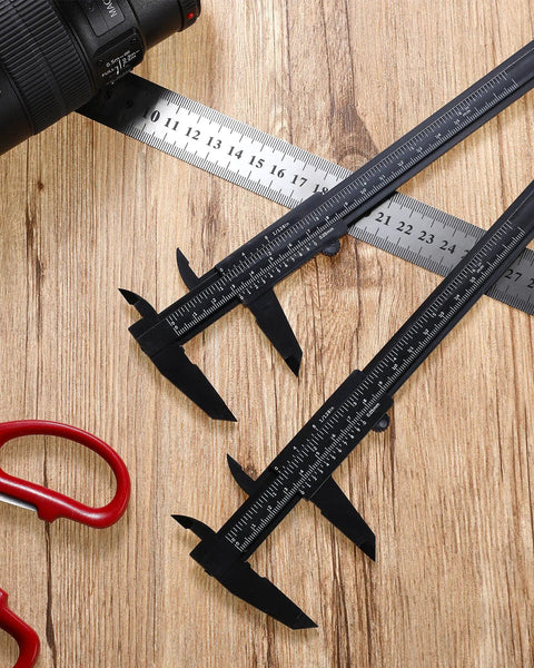 Three black 6 inch 150 mm dual scale vernier calipers on wooden surface with a camera lens and scissors nearby.