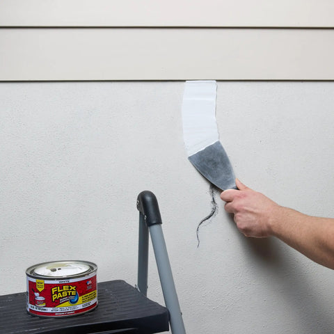 Heavy Duty Rubberized Waterproof Sealant Paste In Bright White Half Quart Tub applied with a putty knife on a wall seam.