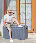 Person sitting on Huge 100 Gallon Outdoor Resin Deck Box With Lockable Lid For Patio Furniture Cushions Garden Tools And Pool Supplies Waterproof Weatherproof Storage With Large Capacity Dark Grey.