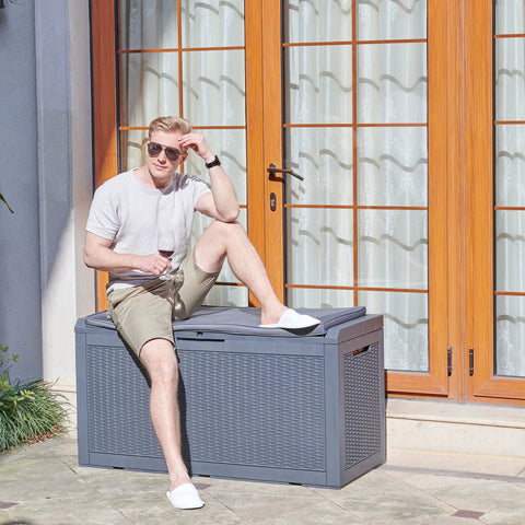 Person sitting on Huge 100 Gallon Outdoor Resin Deck Box With Lockable Lid For Patio Furniture Cushions Garden Tools And Pool Supplies Waterproof Weatherproof Storage With Large Capacity Dark Grey.