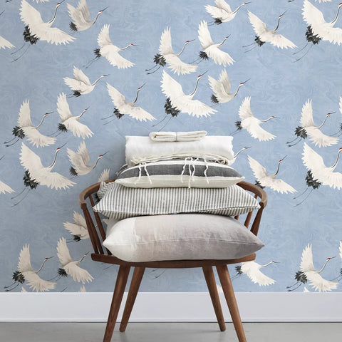 Chair with cushions in front of Windsong Crane Wallpaper Periwinkle, Unpasted Nonwoven, 10.4-Inch Repeat, Hand-Painted Crane Motif