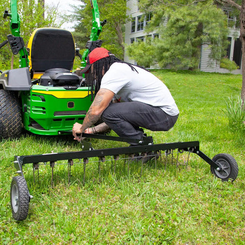 Tow Behind 48 Inch Grass Dethatcher for Big Lawns being attached to a green ride-on mower on grass