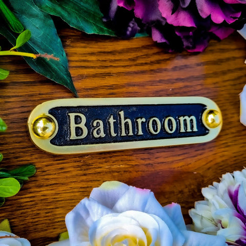 Brass bathroom sign on wooden background with flowers, similar to 'No Soliciting Brass Door Sign For A Chill Home Traditional Style Wall Plaque Handcrafted Metal Decor'
