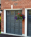 Level Up Your Porch With This Classic Jelly Jar Outdoor Wall Light In Sleek Matte Black Featuring Wet Rated Durability And Fully Dimmable Ribbed Glass For Smooth Lighting Vibes All Season Long by a garage with a hanging flower basket.