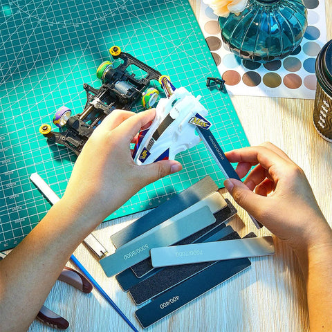 Person using 40 Pcs Polishing And Sanding Sticks For Metal Wood Plastic Models Buffing Kit on a plastic model car.