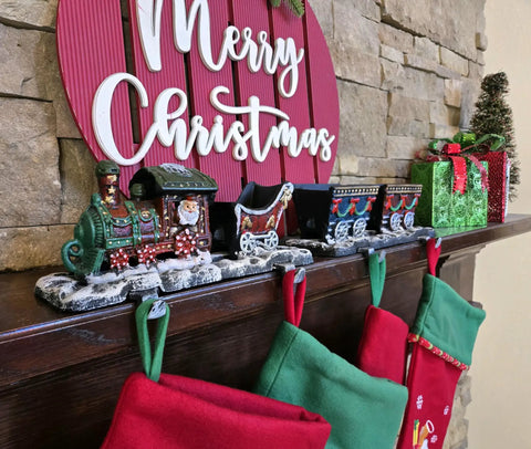 Top Shelf Cast Iron 3D Train Christmas Stocking Holder With Santa Sleigh And Four Rail Carts Six Stocking Hooks above red and green stockings.