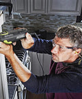 Man using AW400 F80 Sonicrafter 4.2 Amp Oscillating Multi Tool With 9 Accessories And Carry Bag, cutting wood trim in kitchen.