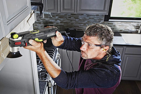Man using AW400 F80 Sonicrafter 4.2 Amp Oscillating Multi Tool With 9 Accessories And Carry Bag, cutting wood trim in kitchen.