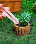 Handheld Seed Spreader And Manual Planter Tool With Ergonomic Grip being used in a garden with small potted plant, precise planting