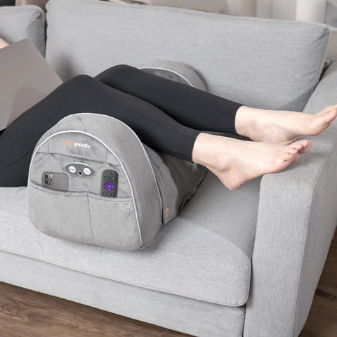 Carepeutic Contoured Leg Rest Wedge With Vibration Massage And Heat on gray sofa, supporting user’s legs with remote controls and soft touch surface.