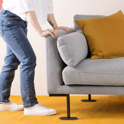Person moving a gray sofa on Sixteen Piece 6 Inch Oval Furniture Sliders For Carpet Glide Heavy Sofas Chairs Tables And More Across Carpeted Floors With Ease Padded Moving Pads For Floor Protection No Scratches Mover Pack, showing ease of use on carpet.