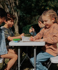 Children playing at a Compact Kids Picnic Table With Foldable Benches Under The Table And Built In Carry Handle For Easy Transport