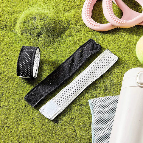 Black and white jersey sleeve bands with hook and loop fasteners for shirts, shown on a green surface with sports accessories.