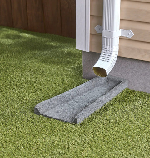 Heavy Duty Two Pack Premium Rubber Downspout Splash Blocks Built Damn Tough With A Slick Stone Texture For Top Shelf Yard Drainage And Clean Rainwater Management In Gray positioned under gutter outlet on grass.