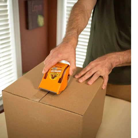Person sealing a box with Ultra Thick And Wide Packing Tape With Dispenser For Moving Shipping And Storage Tough As Nails Crystal Clear 2.83 Inch By 35 Yard Tape Six Roll Pack Easy To Cut Smooth Quiet Dispensing Moisture And Temperature Resistant.